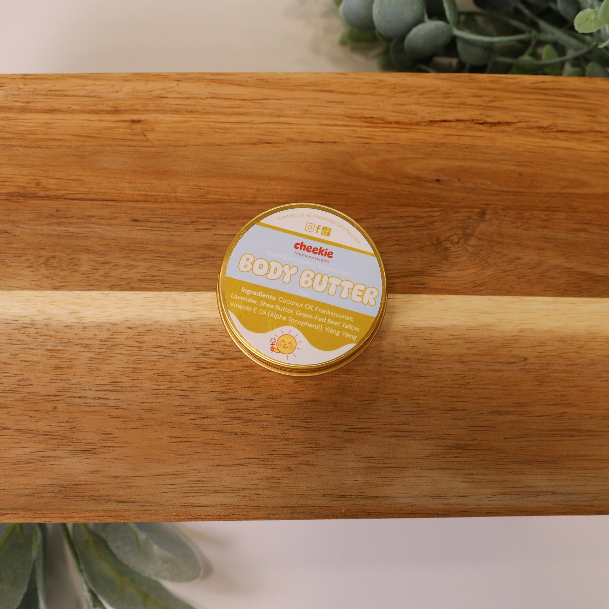 Body butter container on a wooden surface with greenery in the background