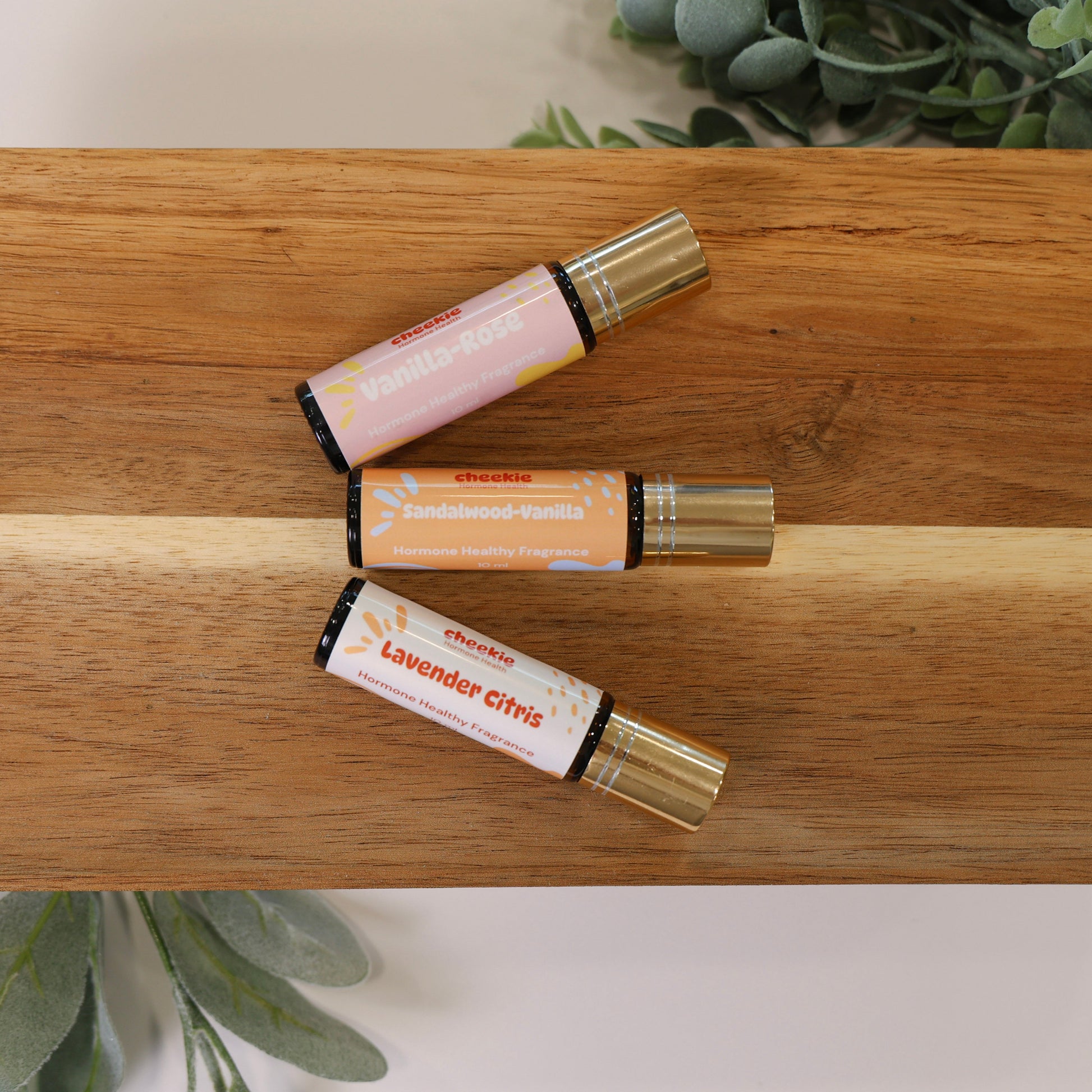 Three rollerball bottles on a wooden tray with greenery in the background