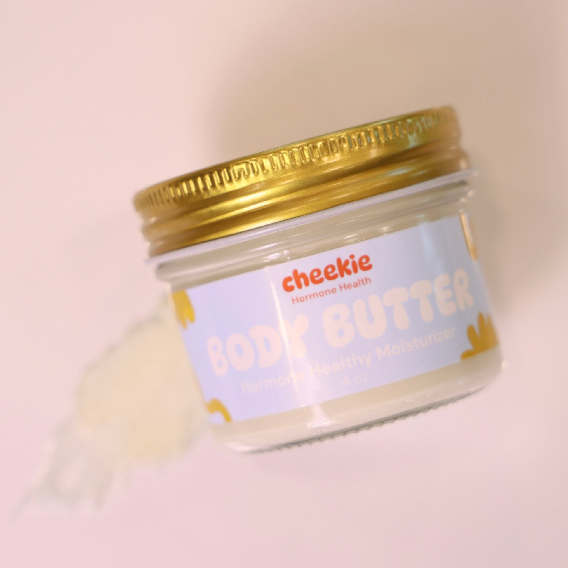 Jar of body butter with a gold lid on a light pink background