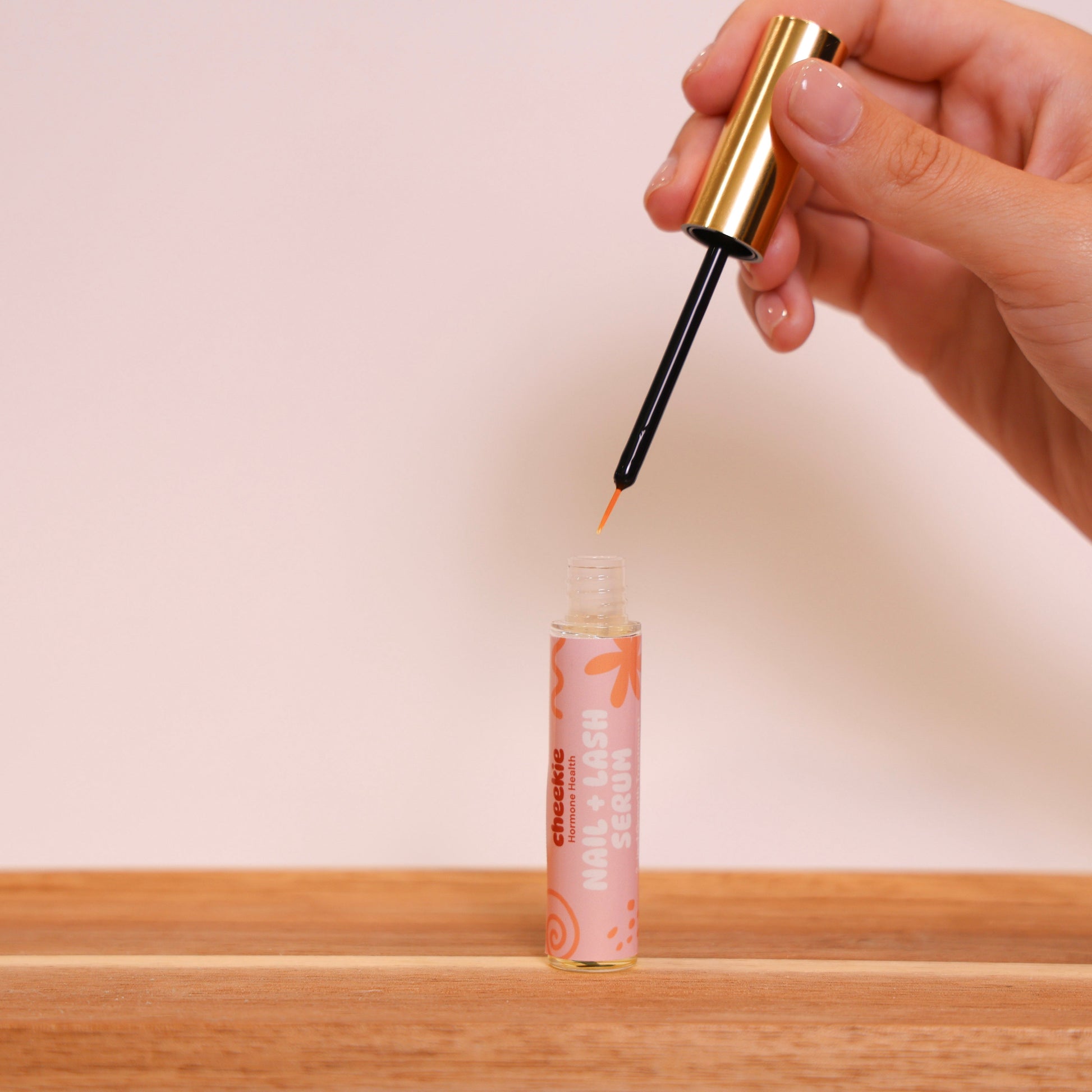 Hand holding a dropper over a small bottle on a wooden surface with a plain background