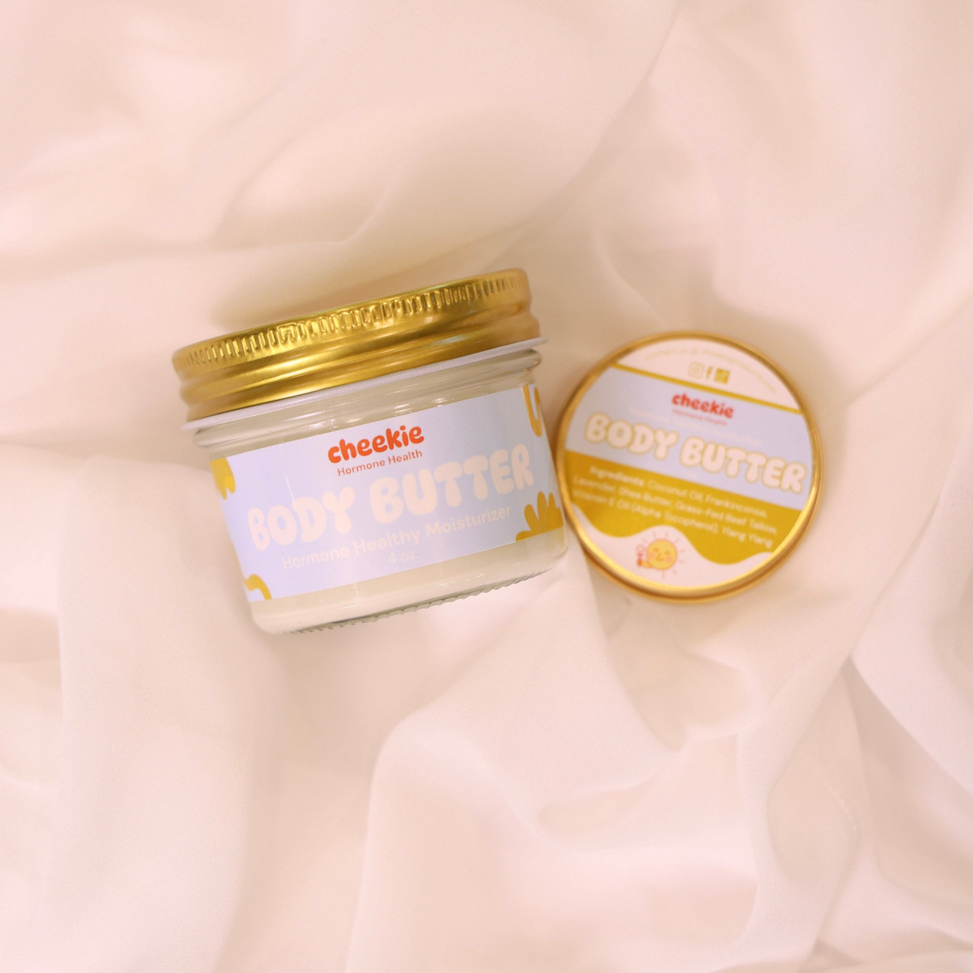 Two jars of body butter on a soft, light-colored fabric background